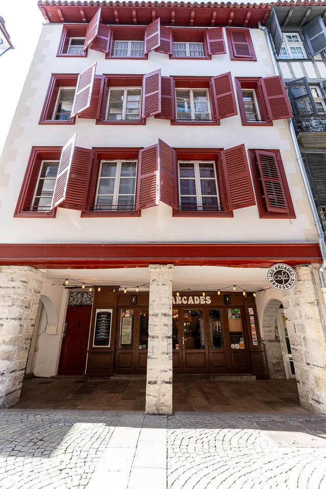 Façade basque rénovée avec arcades en pierre et volets rouges